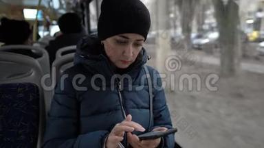 特写镜头，一个手里拿着手机的成年女孩正坐在一辆公交车的窗口，温暖地穿过城市